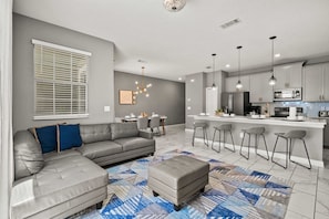Un salon moderne avec un canapé d’angle, un pouf et un tapis à motifs.