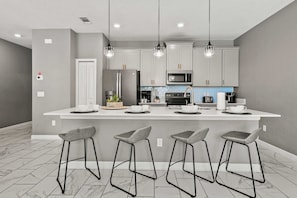 Une cuisine moderne dotée d’un îlot central, de tabourets de bar et de luminaires suspendus.
