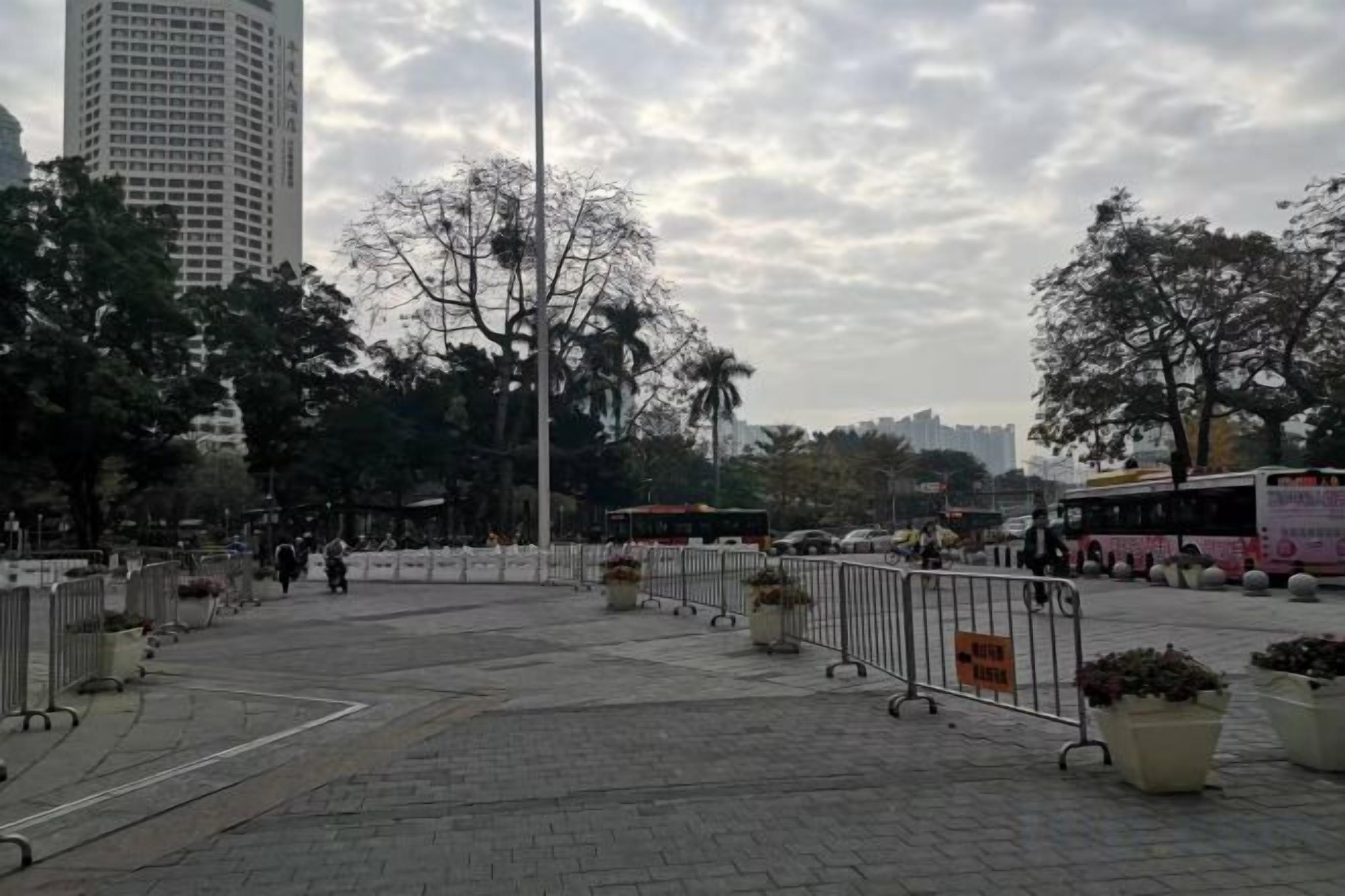 Un espacio urbano al aire libre con senderos pavimentados, barreras metálicas y plantas en macetas.