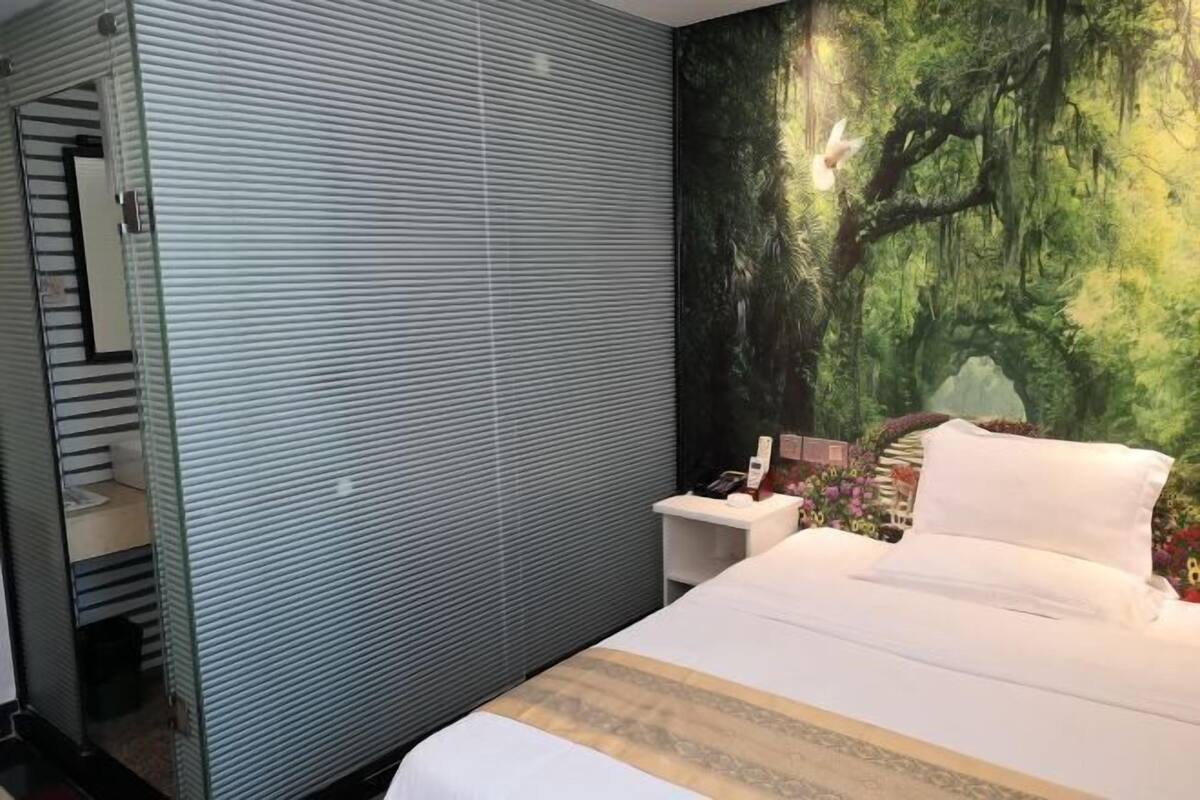 A hotel room with a bed, a nightstand, a telephone, and a mural of a forest scene.
