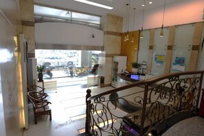 Vestíbulo de hotel con escalera, zona de estar y mostrador de recepción.