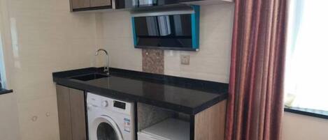 A compact kitchen with a washing machine, a sink, and a microwave.