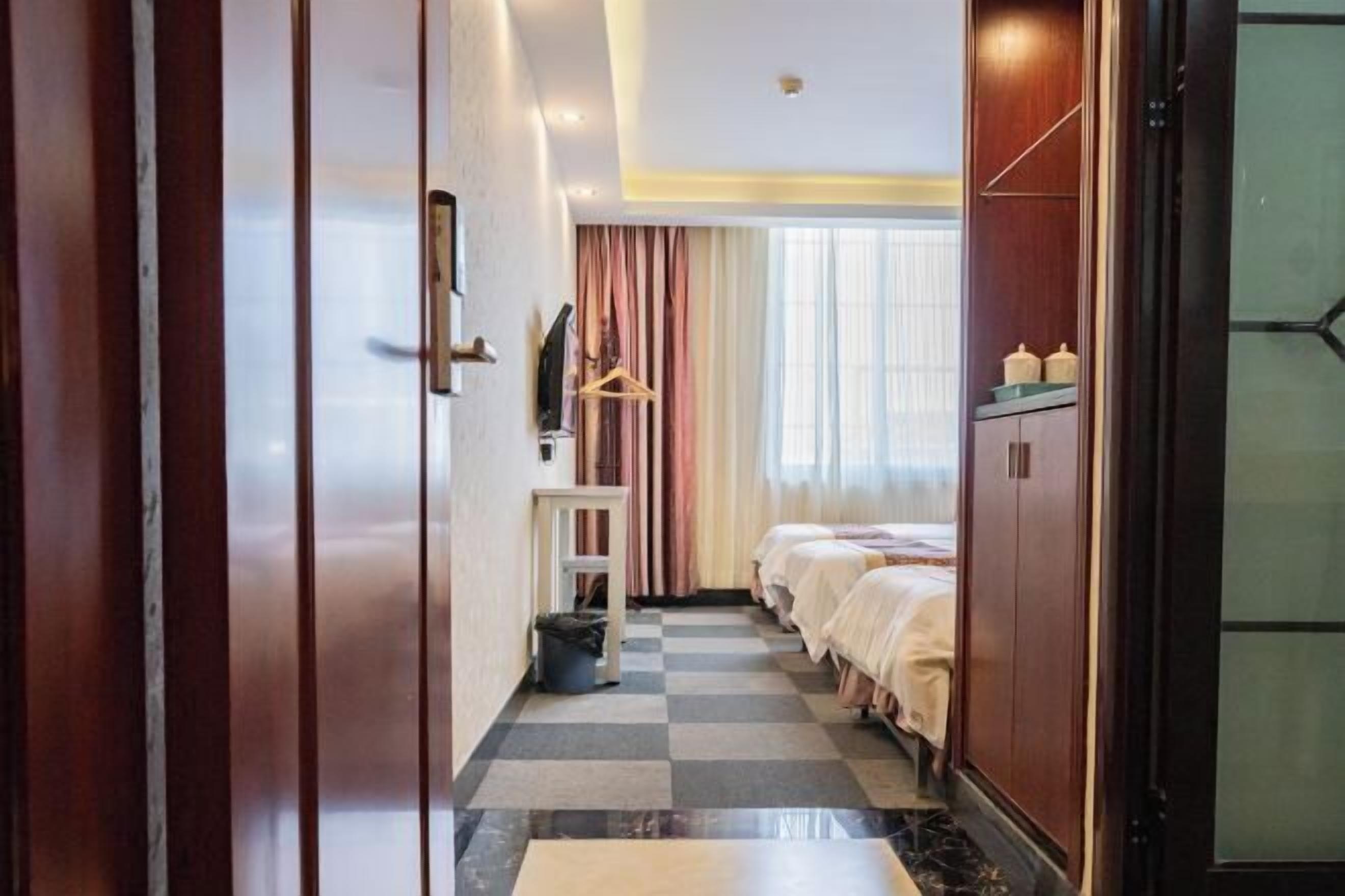 A hotel room with a checkered floor, a bed, a wardrobe, and a small table with a hanging garment rack.
