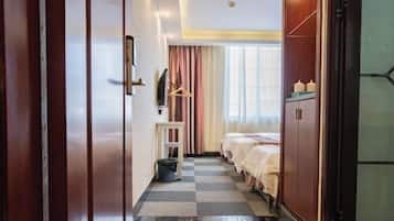 A hotel room with a checkered floor, a bed, a wardrobe, and a small table with a hanging garment rack.