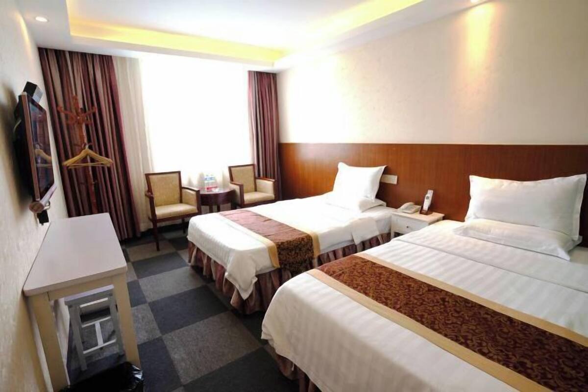 A hotel room with two beds, a desk, a chair, a small table, and a TV.