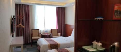 A hotel room with two beds, a desk, a chair, a small table, and a window with curtains.