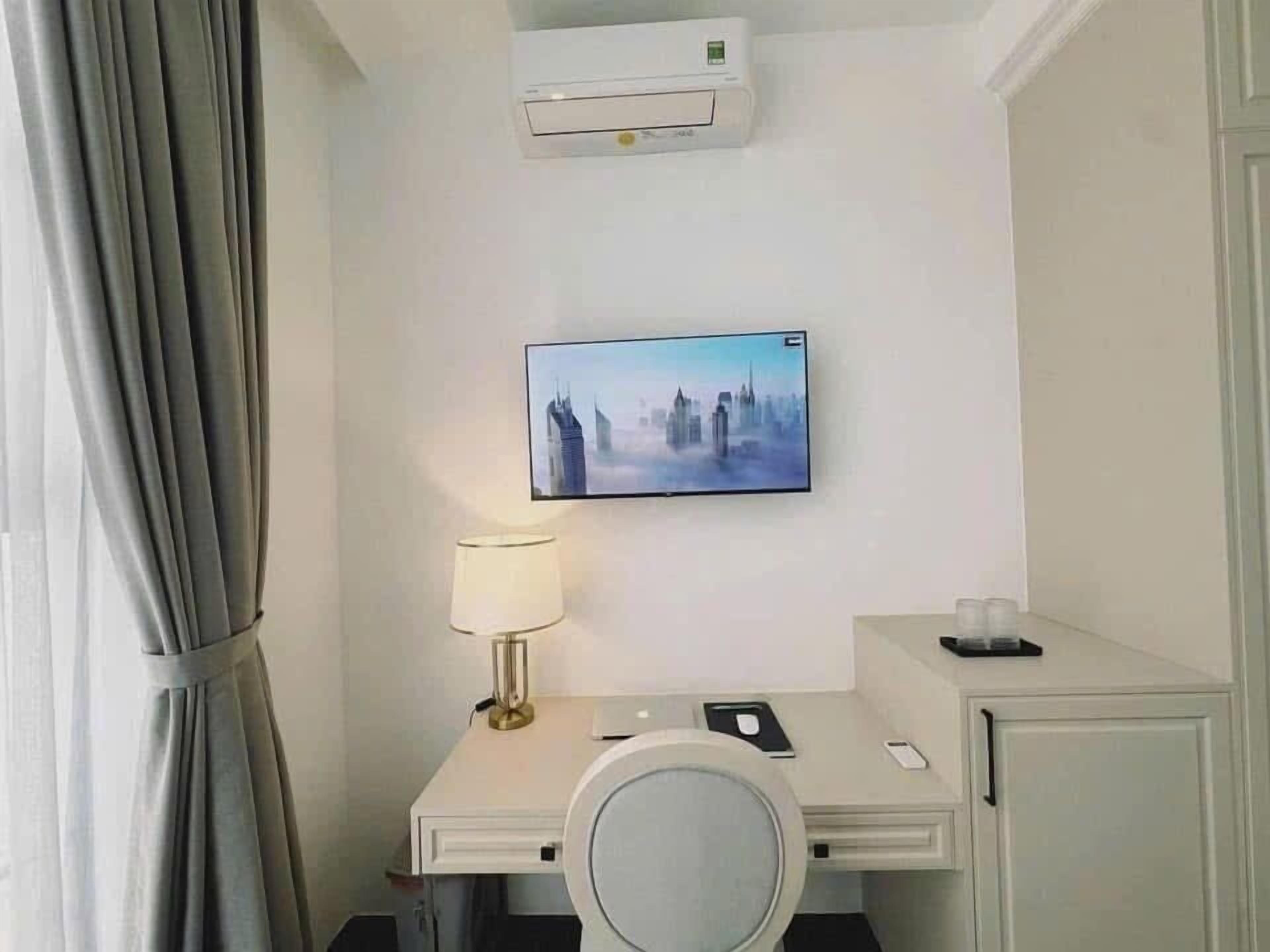 Een hotelkamer met een bed, een nachtkastje met lamp, een aan de muur bevestigde televisie en een airconditioner boven het bed.
