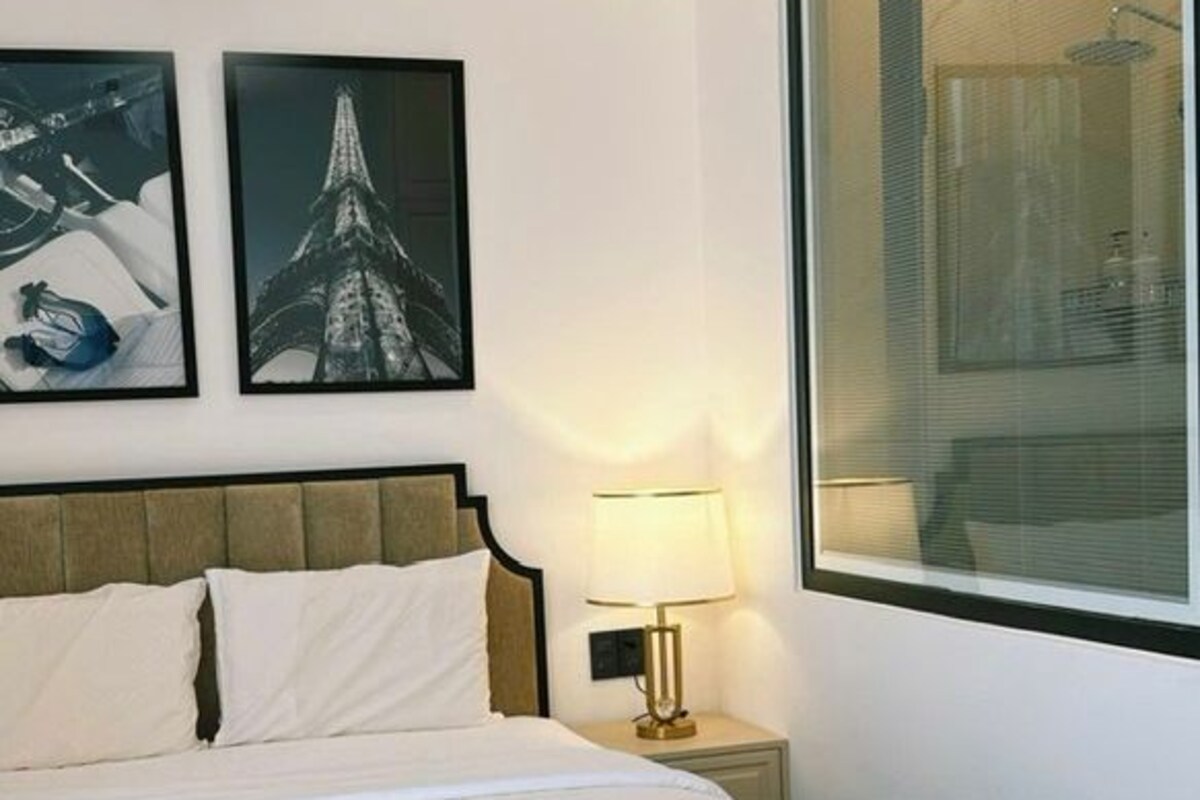 A hotel room with a bed, a nightstand, a lamp, and two framed pictures on the wall.