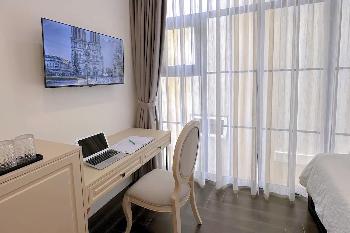 Une chambre d’hôtel équipée d’un bureau, d’une chaise, d’un lit, d’une télévision et de rideaux.
