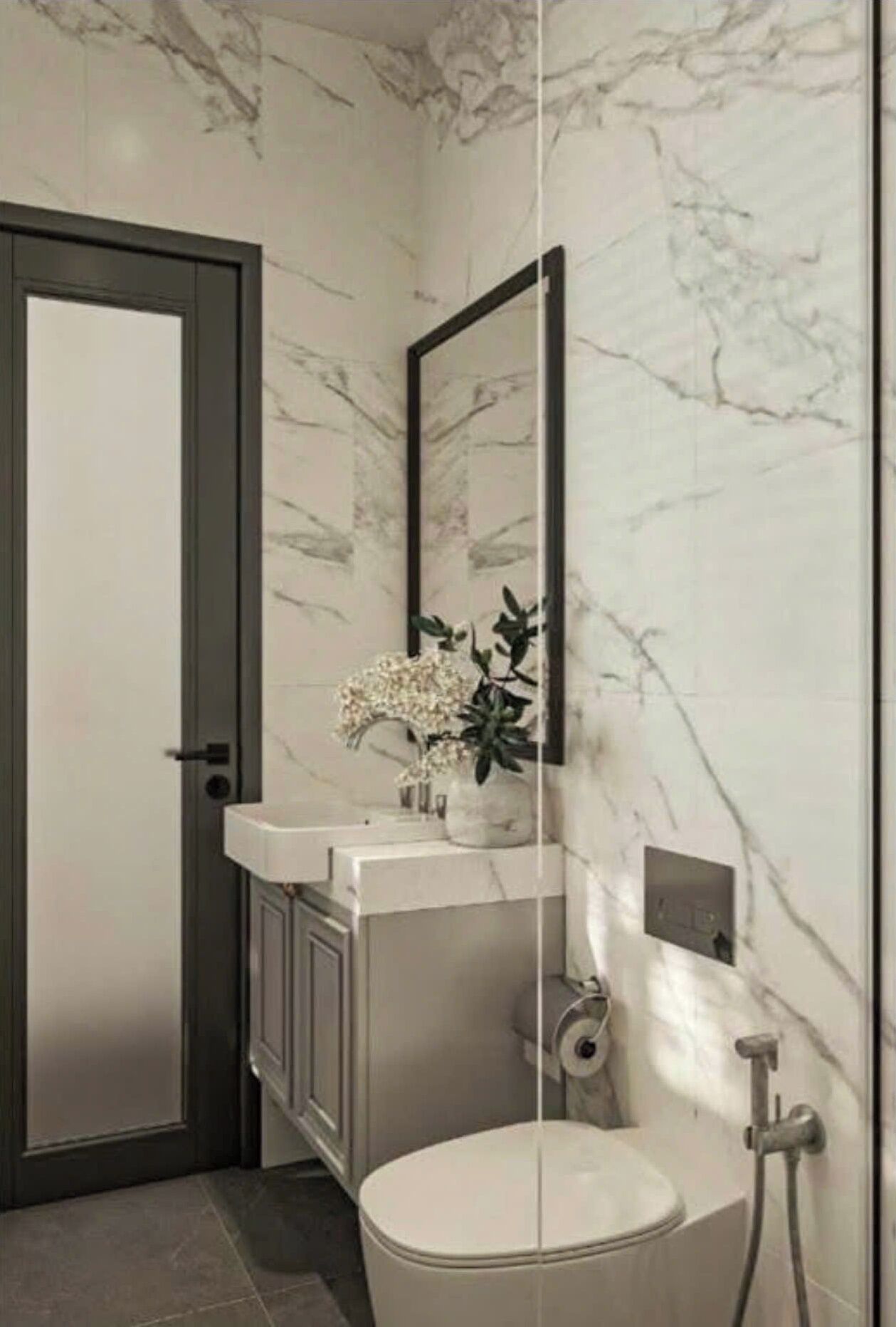A bathroom with a marble wall, a toilet, a sink with a mirror, and a shower.