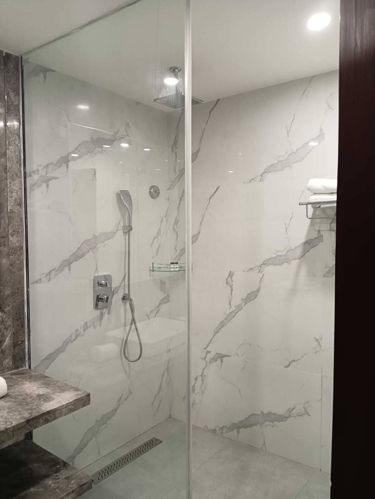 A modern bathroom with a glass-enclosed shower, marble walls, and a visible towel rack.