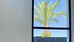 Un soggiorno moderno con due divani grigi, un tavolino in legno e una grande finestra che si affaccia su una palma e un giardino recintato.