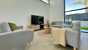 Un soggiorno moderno con due divani grigi, un tavolino in legno, una televisione a schermo piatto e un'ampia finestra con vista su una palma e un edificio.