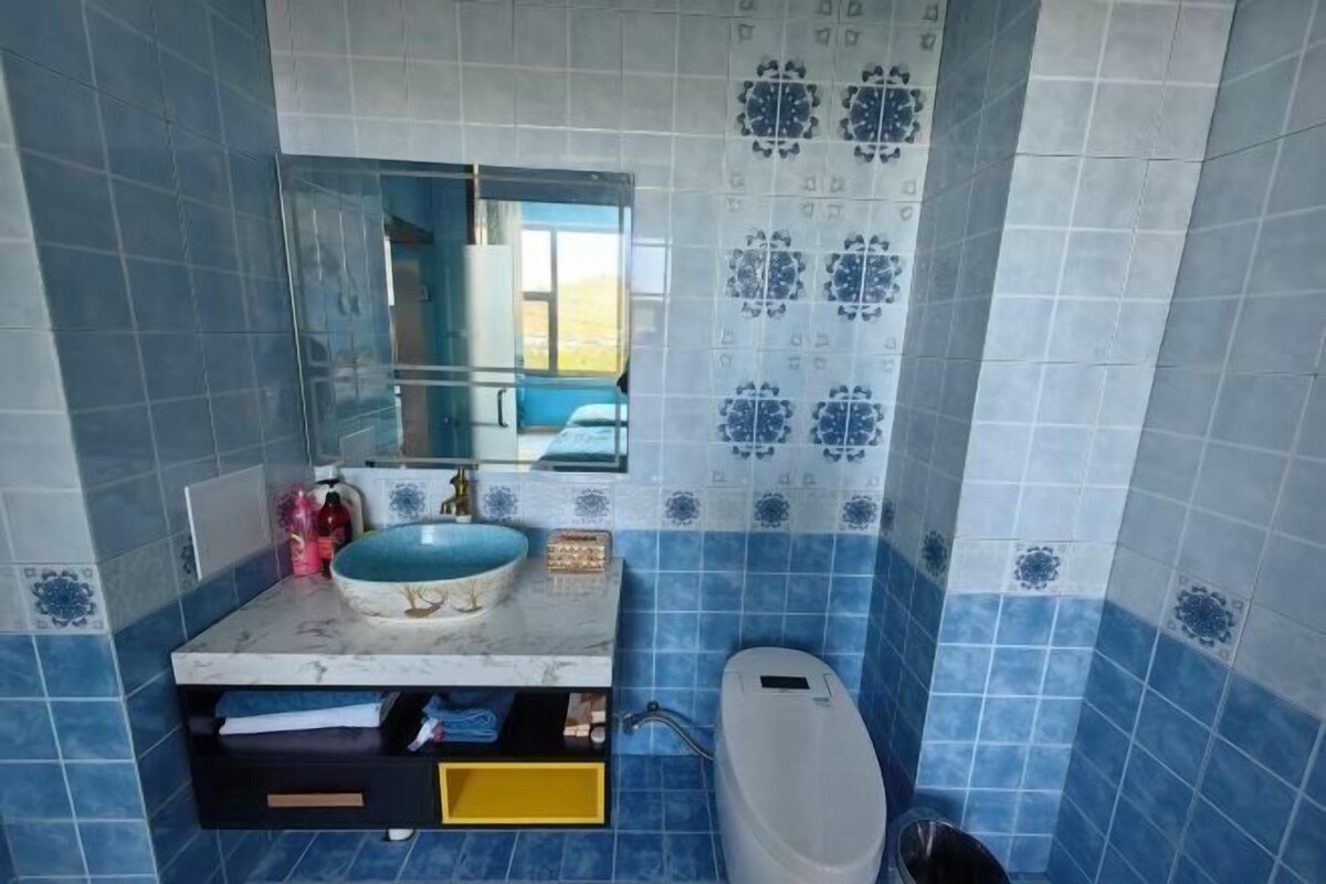 A bathroom with blue tiles, a sink with a marble countertop, a mirror, and a toilet.