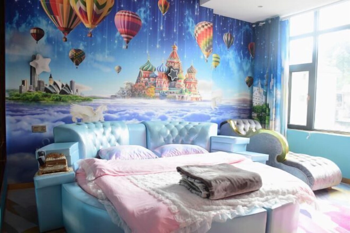 A bedroom with a mural of a city skyline and hot air balloons, a tufted headboard, and a bedside table with a lamp.