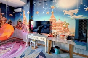 A room with a large flat-screen TV, a white desk, and a colorful mural of a cityscape. - Longling Ocean Theme Hotel (Longling)