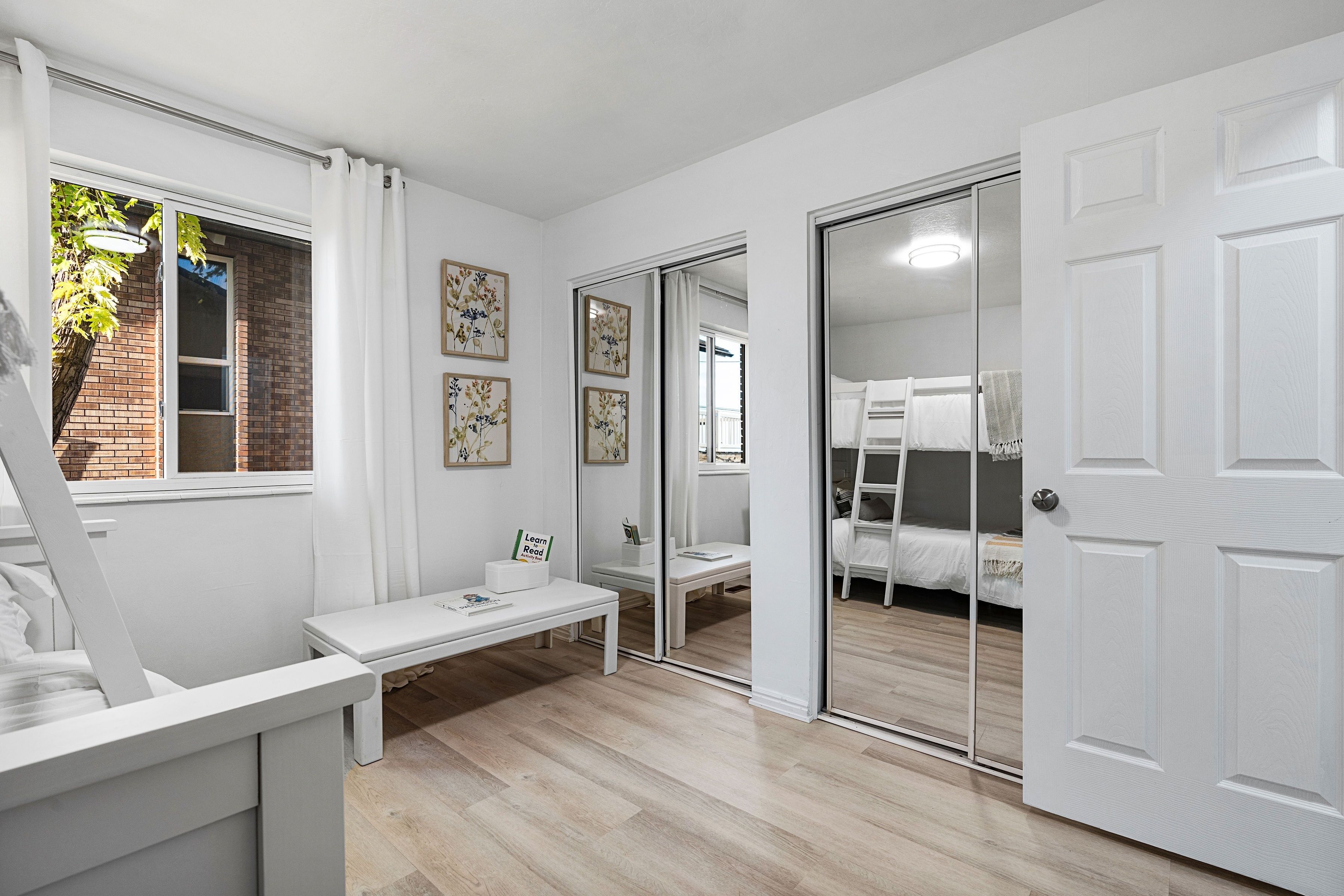 A modern bedroom with a large bed, a bedside table, a bench, and a sliding glass door leading to a balcony.