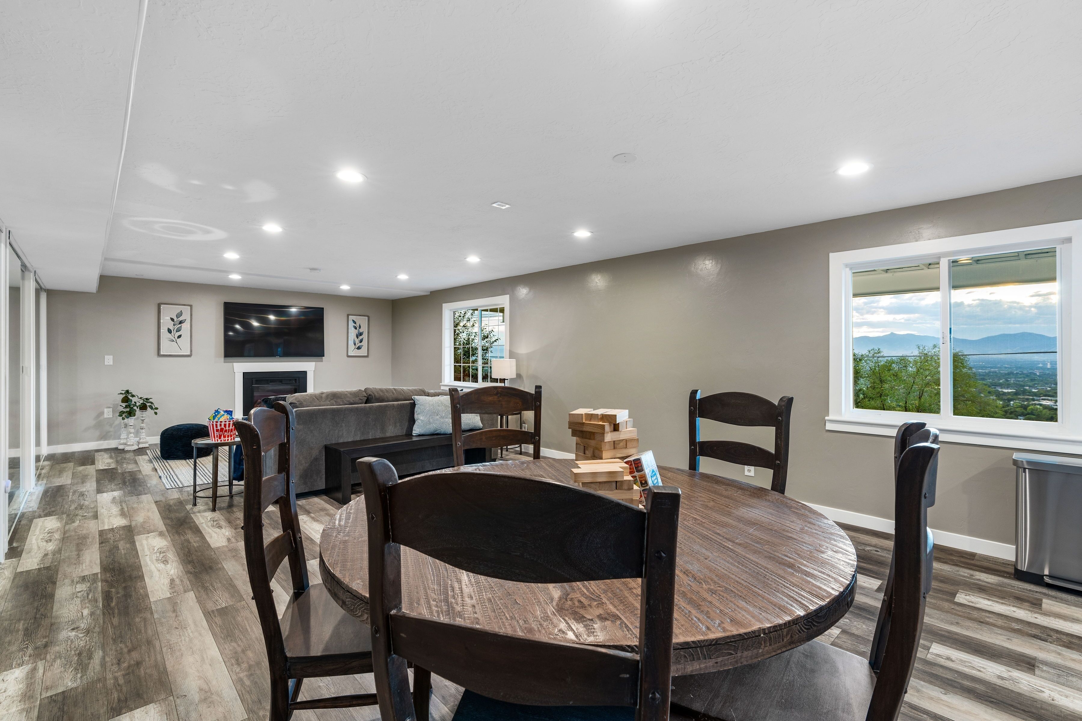 A modern living room with a fireplace, a dining area with wooden chairs, and a large window offering a scenic view.