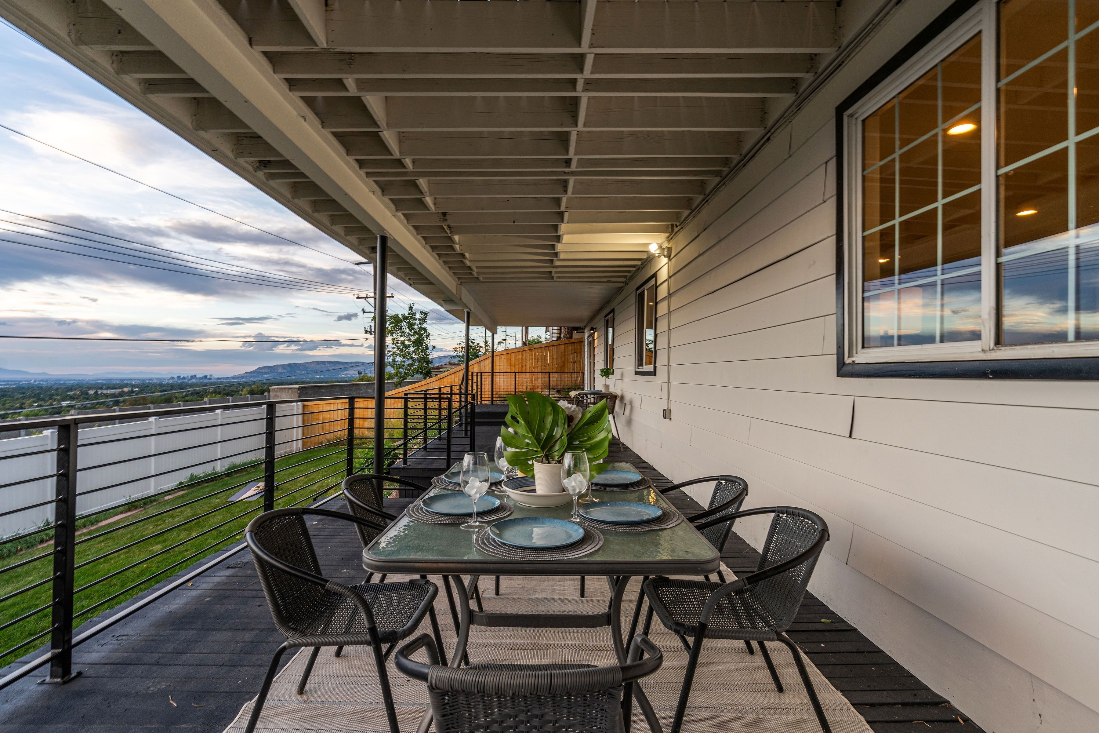 A covered outdoor dining area with a table set for four, surrounded by chairs, and a view of the landscape.