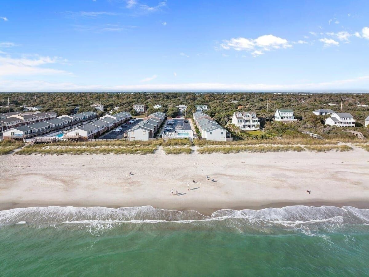 Una vista aerea di una zona residenziale costiera con proprietà sul lungomare, una spiaggia sabbiosa e onde oceaniche.