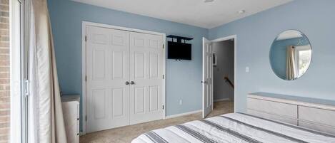 A bedroom with a bed, a ceiling fan, a door, and a wall-mounted TV.