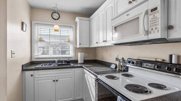 A kitchen with white cabinets, a stove, a microwave, and a window with blinds.