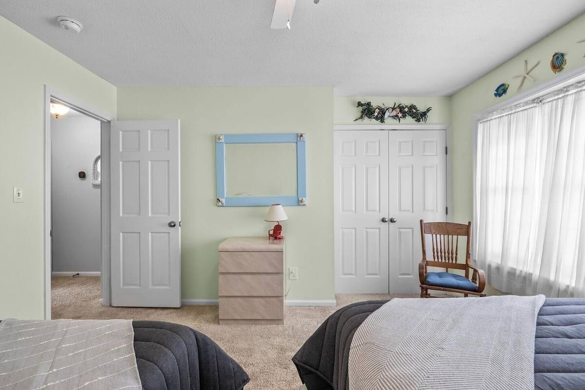 A bedroom with two beds, a dresser, a chair, and a door leading to another room.