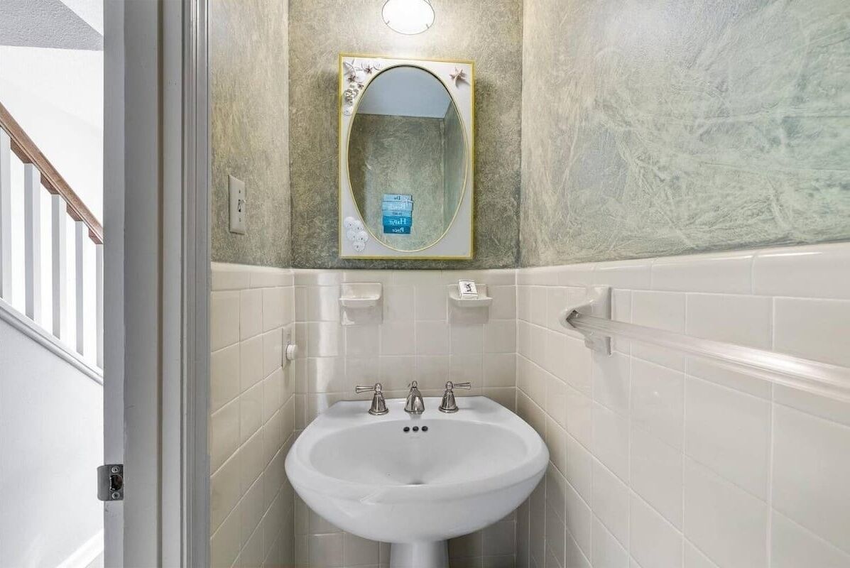 Ein Badezimmer mit einem weißen Waschbecken, einem Spiegel mit Zierrahmen und einer strukturierten Wand.