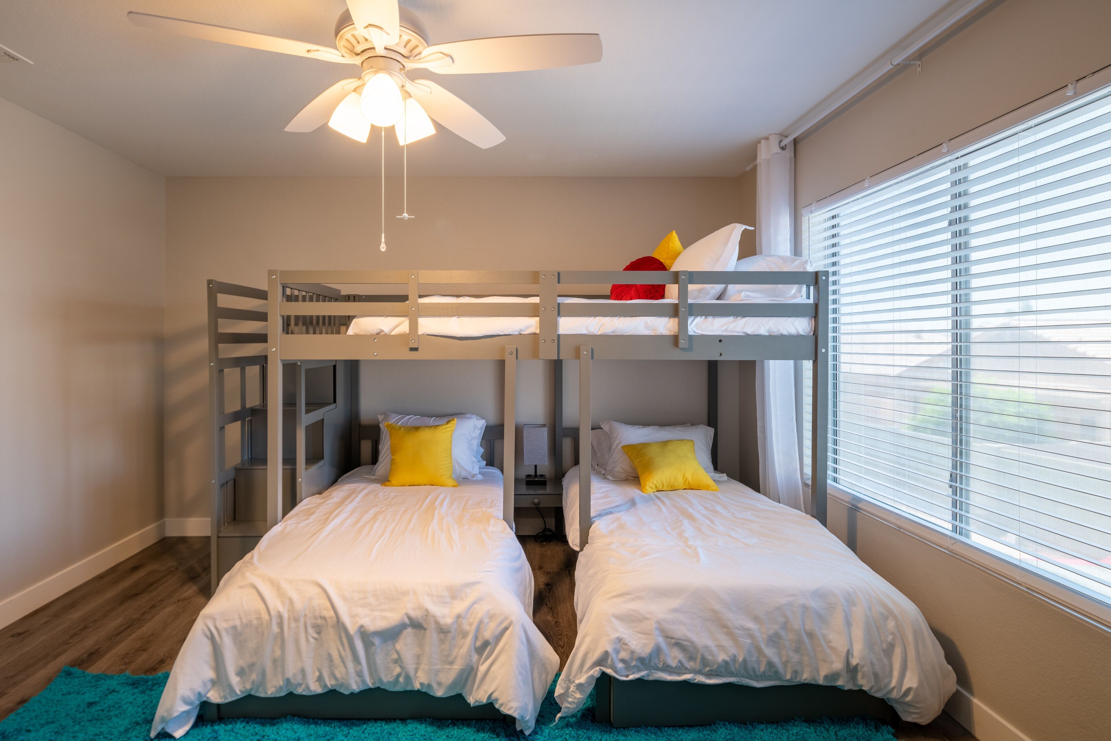 Une chambre avec deux lits superposés, un ventilateur de plafond et une fenêtre avec des stores.