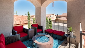 Un balcon agrémenté de meubles en osier, de coussins rouges, d’un jacuzzi avec un bord en verre et d’une plante en pot.