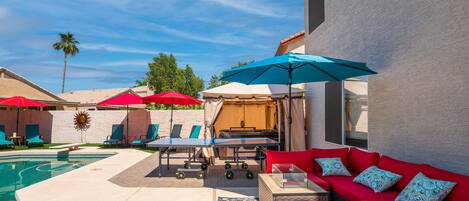 A poolside area with lounge chairs, umbrellas, and a red sofa with patterned cushions.