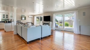 A spacious living room with a large sofa, a fireplace, and a sliding glass door leading to a balcony. - 5BR Cape Cod Retreat, Short Walk to Beach (West Yarmouth)