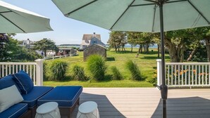 A deck with outdoor seating, a large umbrella, and a view of a house and landscape. - 5BR Cape Cod Retreat, Short Walk to Beach (West Yarmouth)