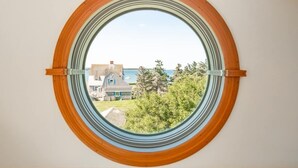 A round window with a view of a house and trees. - 5BR Cape Cod Retreat, Short Walk to Beach (West Yarmouth)