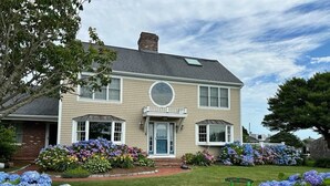 A two-story house with a front porch, a circular window above the door, and a brick chimney. - 5BR Cape Cod Retreat, Short Walk to Beach (West Yarmouth)