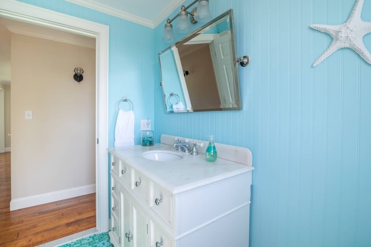 A bathroom with a white vanity, two sinks, a mirror, and a starfish decoration on the wall.