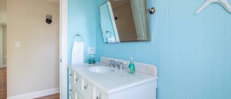 A bathroom with a white vanity, two sinks, a mirror, and a starfish decoration on the wall.