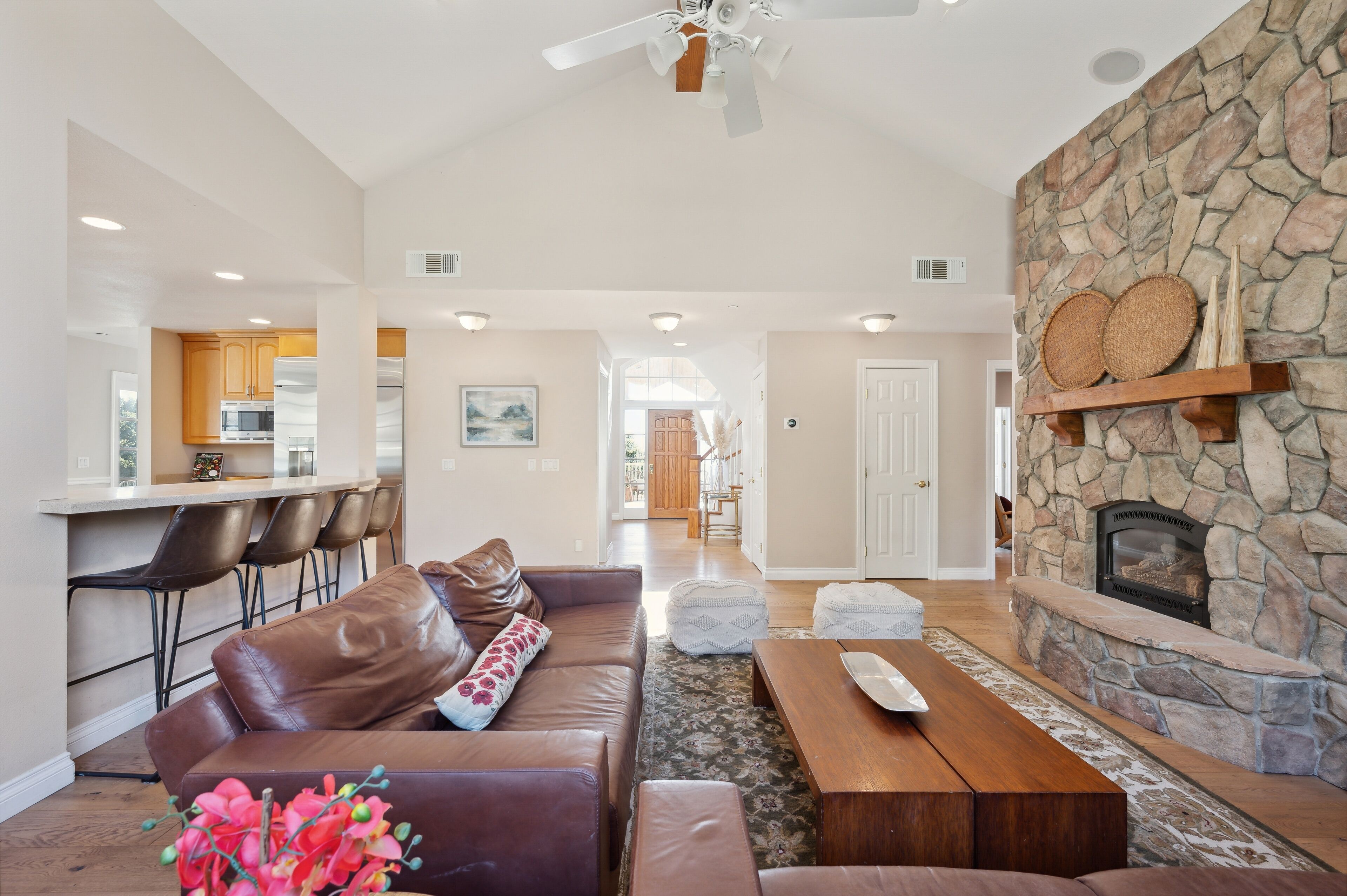 A spacious living room with a stone fireplace, leather sofa, and a dining area with bar stools.