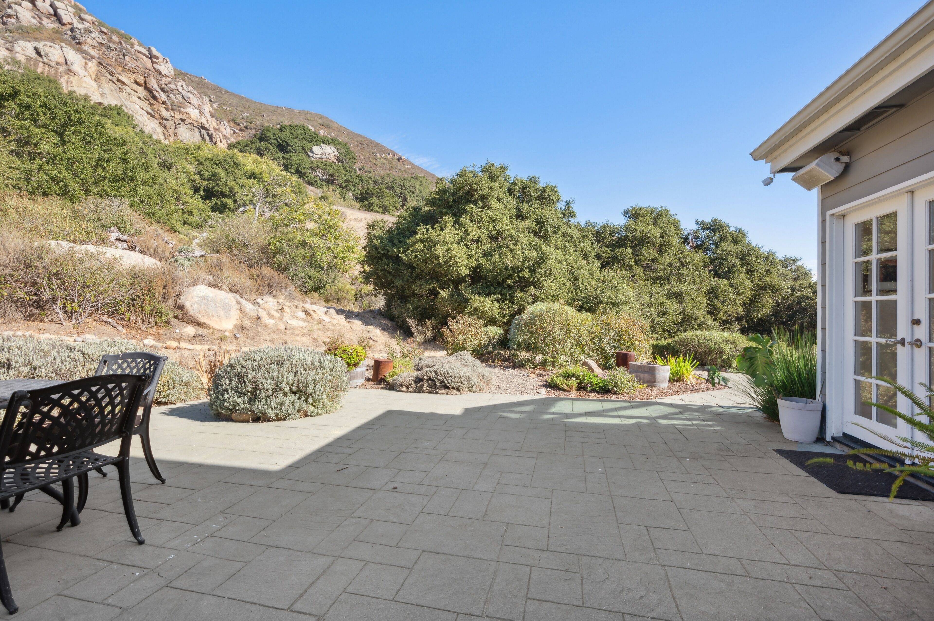 A patio area with a table and chairs, surrounded by potted plants and a view of a hillside.
