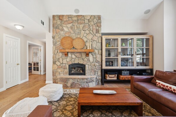 Una sala de estar con chimenea de piedra, un mueble de madera con puertas de cristal y un sofá de cuero marrón.