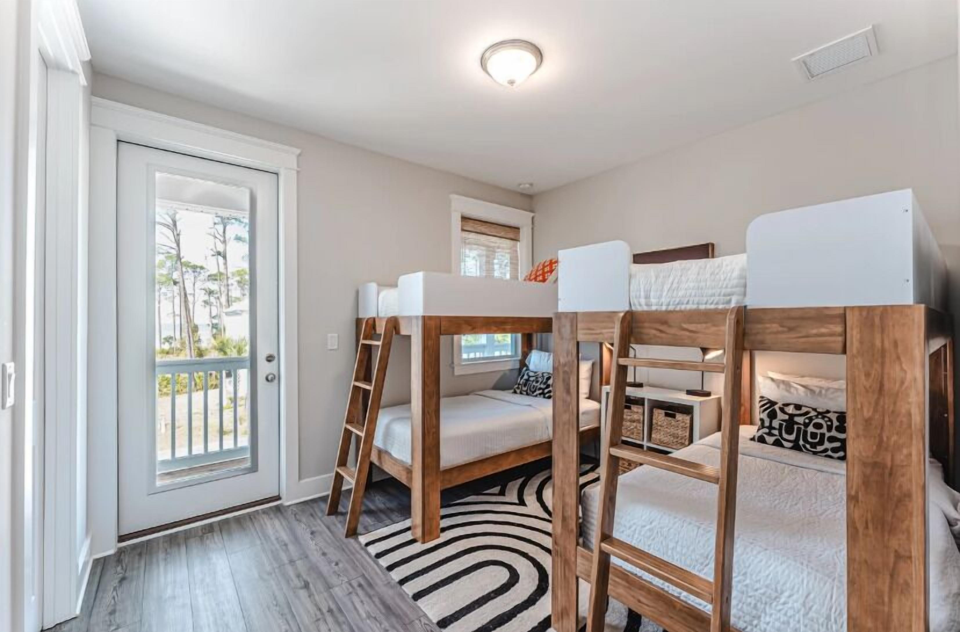 A room with bunk beds, a door leading to a balcony, a small window, and a ceiling light.