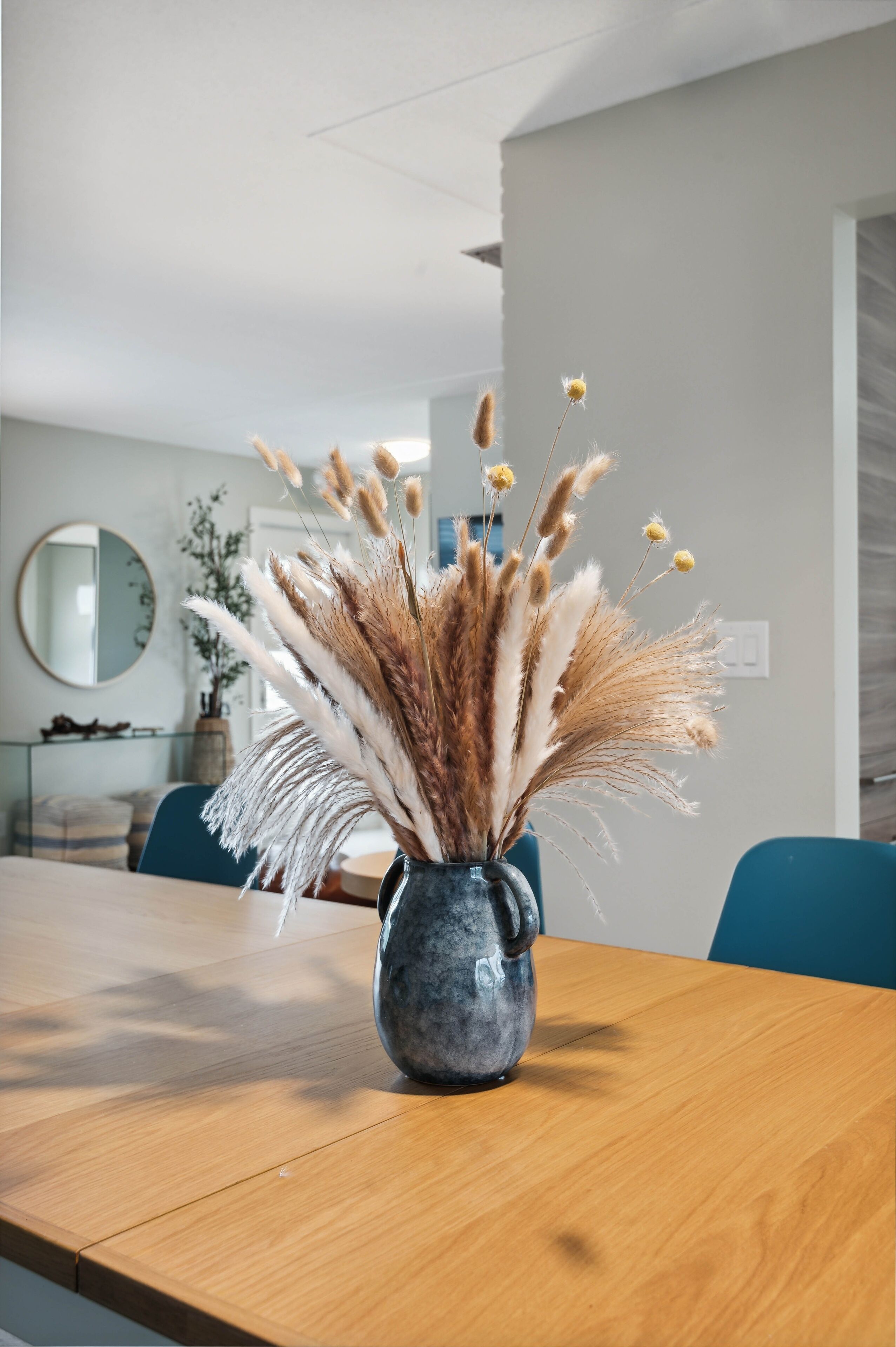 A wooden table with a vase of dried pampas grass and small yellow flowers.