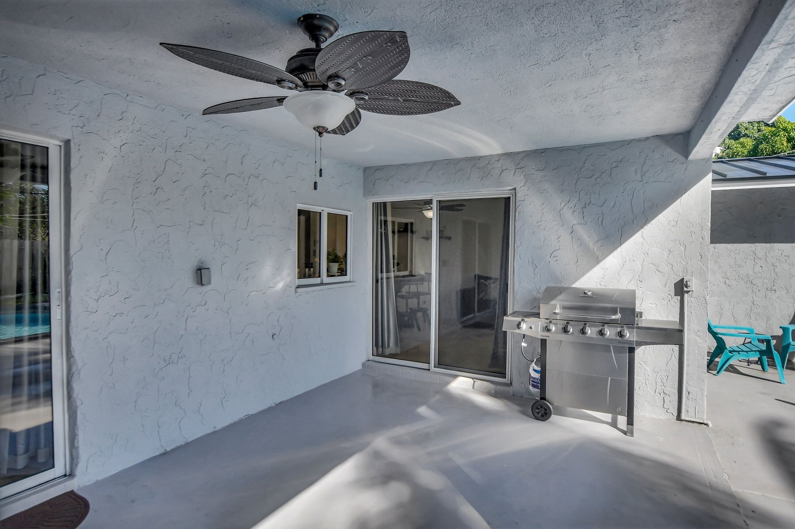 Un espace patio moderne doté d’un ventilateur de plafond, de portes-fenêtres coulissantes et d’un barbecue mobile.