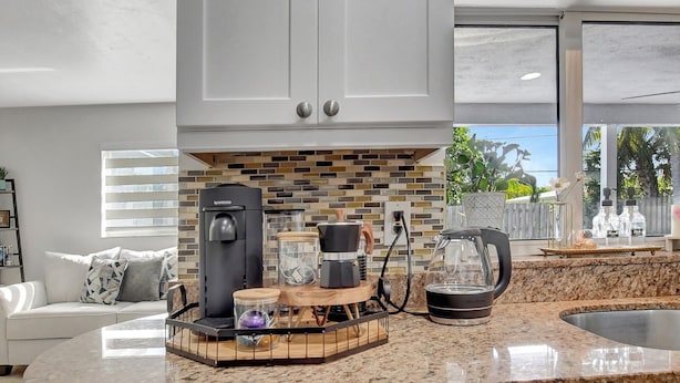 A modern kitchen with white cabinets, a coffee station, and a view of the outdoors. - Boca Beauty - Stylish Home With Pool 3 Bedroom Home by RedAwning (Boca Raton)
