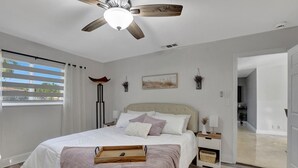 A bedroom with a bed, bedside tables, a ceiling fan, a window with blinds, and a view of the outdoors. - Boca Beauty - Stylish Home With Pool 3 Bedroom Home by RedAwning (Boca Raton)