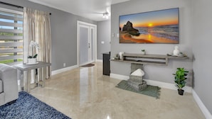 A modern living room with a large painting of a sunset, a grey sofa, a coffee table, and a blue rug. - Boca Beauty - Stylish Home With Pool 3 Bedroom Home by RedAwning (Boca Raton)