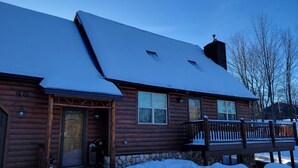 Hirsimökki, jonka perustuksena on kivimuuri, ja jossa on puinen kuisti sekä lumipeitteinen katto.