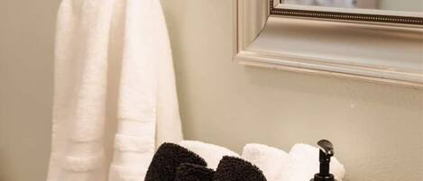 A bathroom with a white towel hanging on a metal towel rack, a wicker basket containing black and white towels, and a bottle of Meyer’s Clean Day hand soap on the countertop.