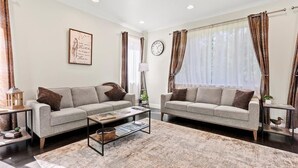 Un salon avec deux canapés, une table basse, une horloge et des rideaux.