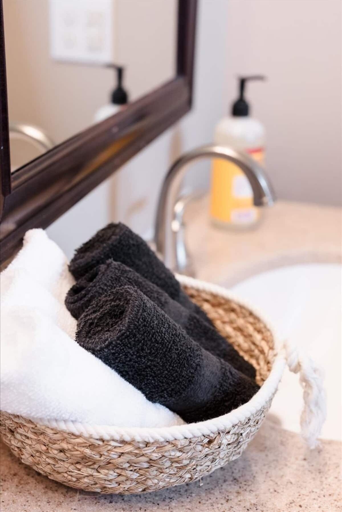 A woven basket with a white towel and two dark towels on a bathroom counter.